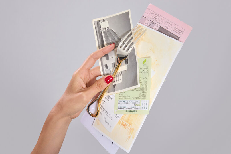 Una mano con esmalte de uñas rojo sostiene un tenedor, algunos papeles, una fotografía en blanco y negro, billetes y formularios sobre un fondo liso.