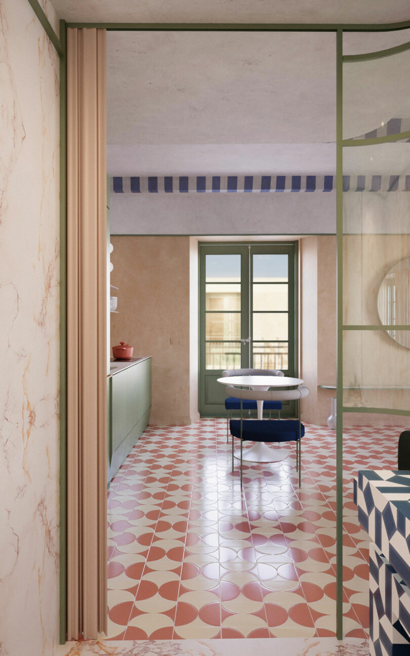 A view into a kitchen with green cabinets, geometric red and white floor tiles, a round table with two chairs, and double glass doors leading to a balcony.