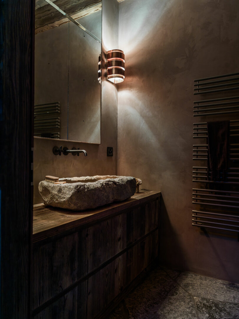 Rustic bathroom with stone sink on wooden vanity, wall tap, large mirror, modern wall light and towel radiator.