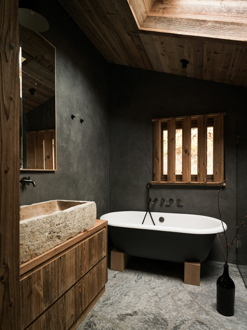 Modern rustic bathroom with stone sink, freestanding tub, wood accents, slate floor and skylight.