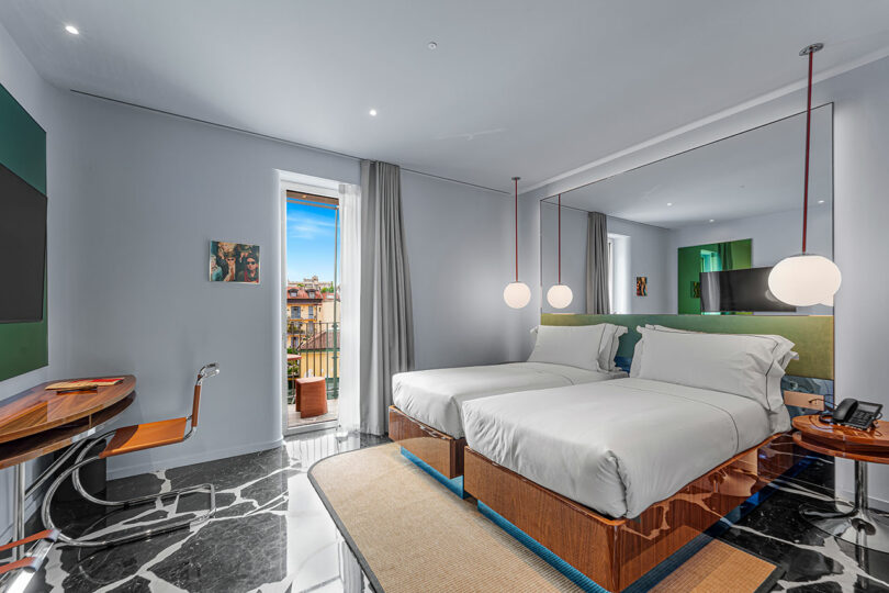 Modern hotel room with two twin beds, a large mirror, desk, TV, marble floor, and a window with a view of a balcony and cityscape.