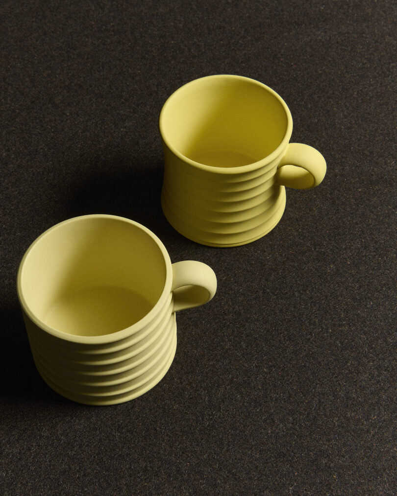 Two yellow ceramic mugs with ribbed exteriors are placed on a dark, textured surface.