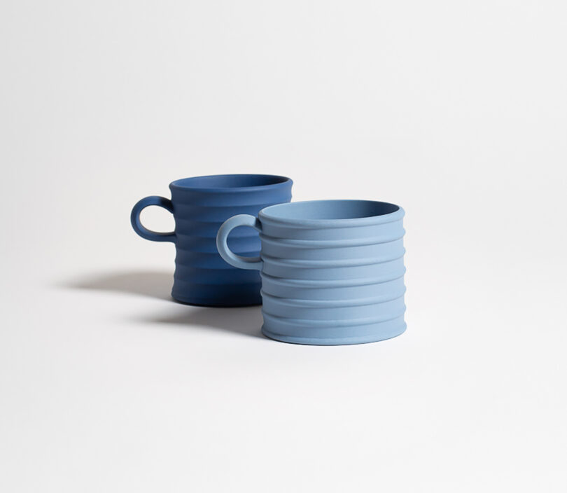 Two blue ceramic mugs with ribbed texture and handles, placed on a plain white surface.