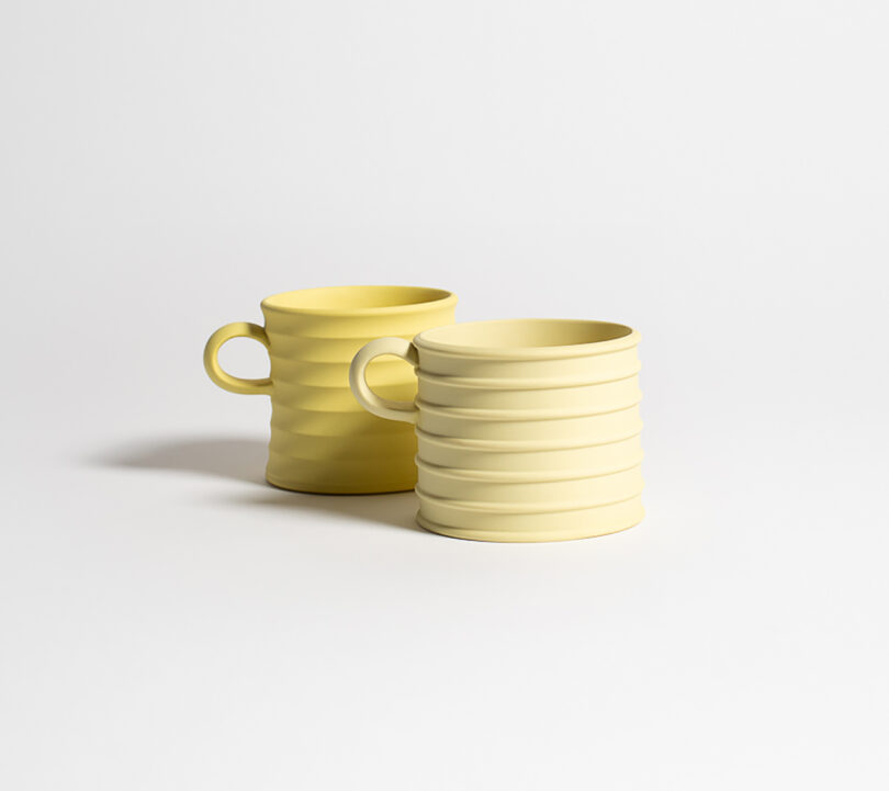 Two yellow ceramic mugs with horizontal ridges and handles are placed on a plain, light background.