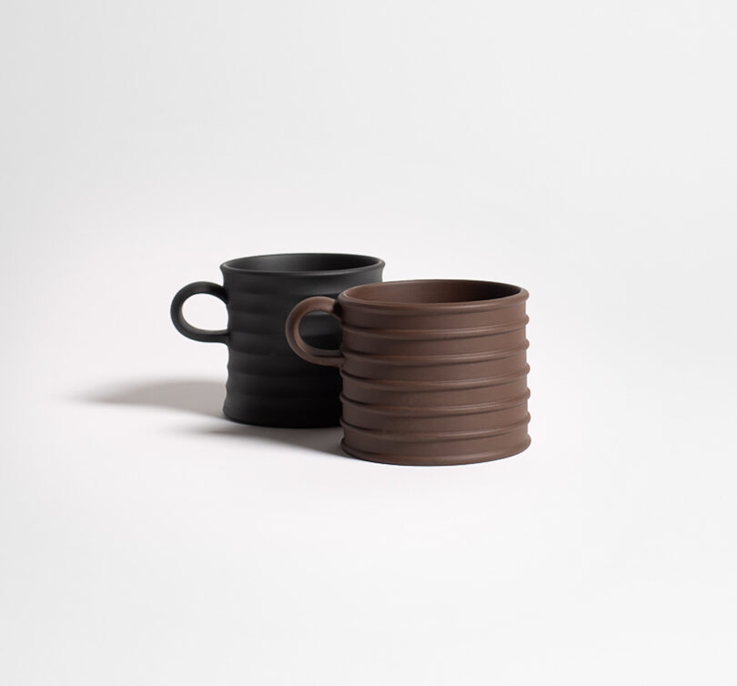Two ribbed ceramic mugs, one black and one brown, placed side by side on a plain white background.