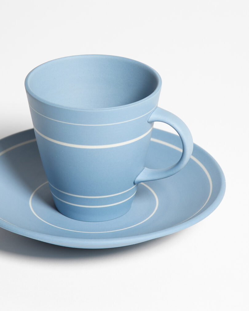 A light blue ceramic cup with white stripes sits on a matching saucer against a plain white background.