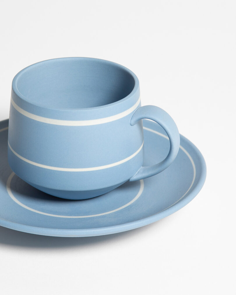 A light blue ceramic cup with white stripes sits on a matching saucer against a plain white background.