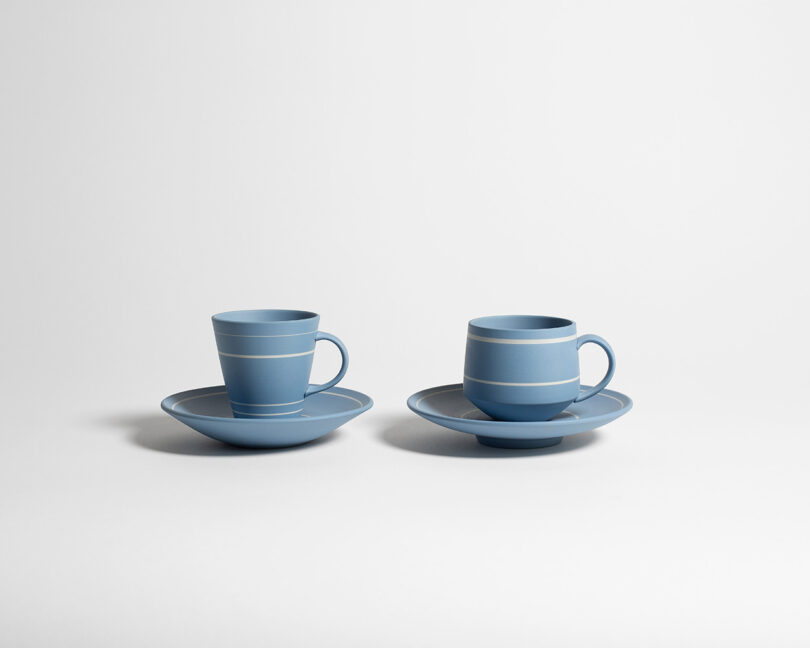 Two blue ceramic cup and saucer sets with white stripes are placed side by side on a plain white surface and background.