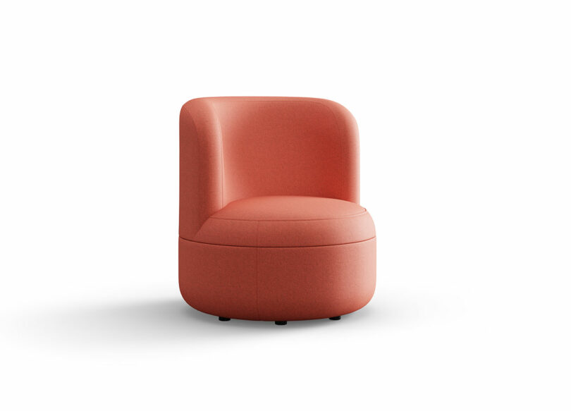 A modern, armless chair upholstered in coral pink fabric, featuring a rounded back and cushioned seat, set against a plain white background.