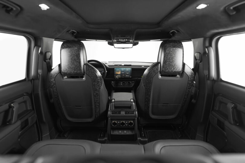 View of a car interior from the back seat, showing two front seats, a dashboard with a touchscreen display, and various controls and vents.