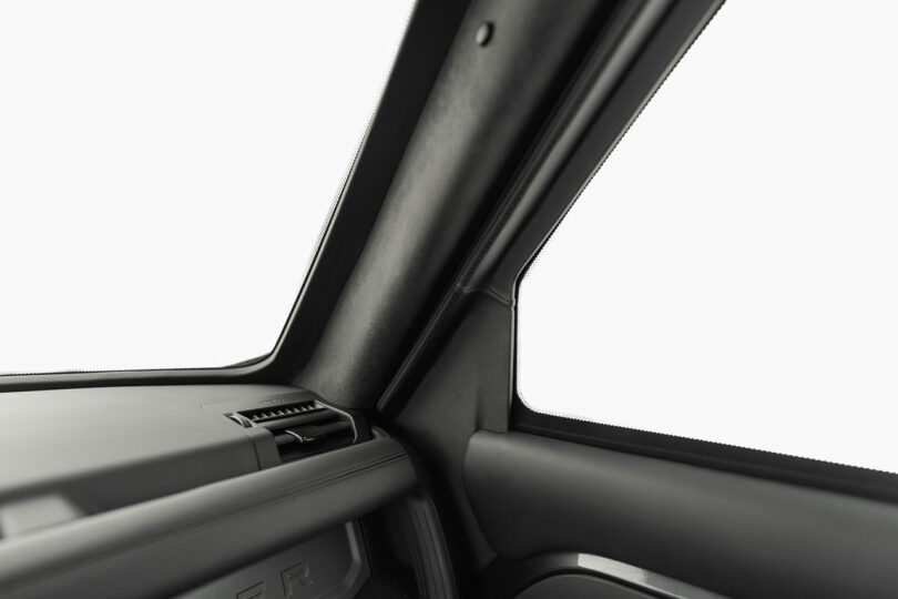 Close-up of a vehicle's interior, showing a section of the dashboard, air vent, and the inside of the windshield with the A-pillar trim.