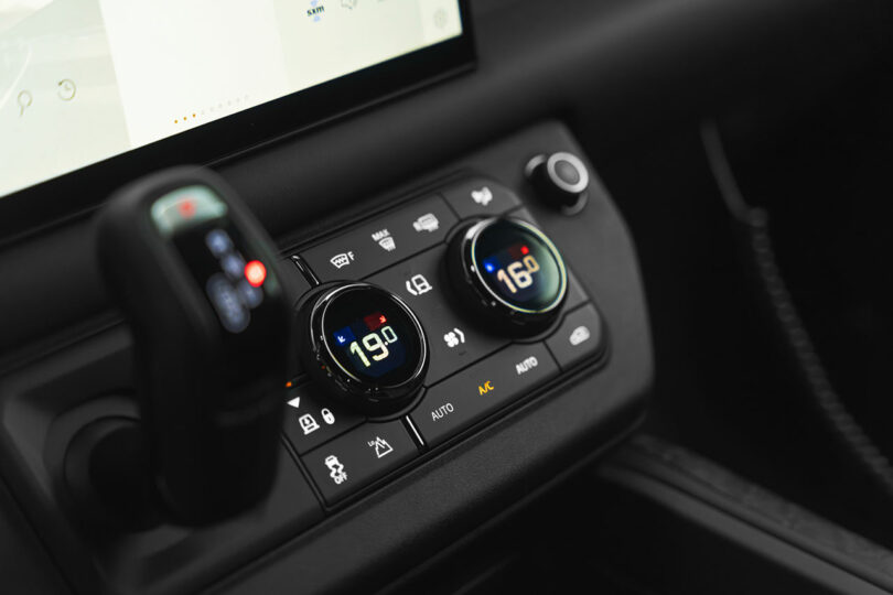 Close-up of a car's digital climate control panel with temperature settings at 19°C and 16°C, gear shifter, and part of a touchscreen display visible.
