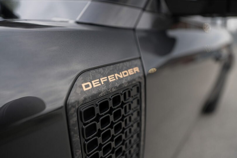 Close-up of a black vehicle with a vent and the word "DEFENDER" in metallic letters on the side panel.