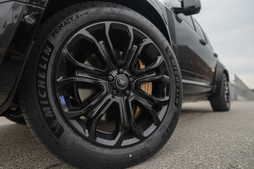 Close-up of a black alloy wheel and Michelin Primacy tire on a dark-colored vehicle parked on asphalt.