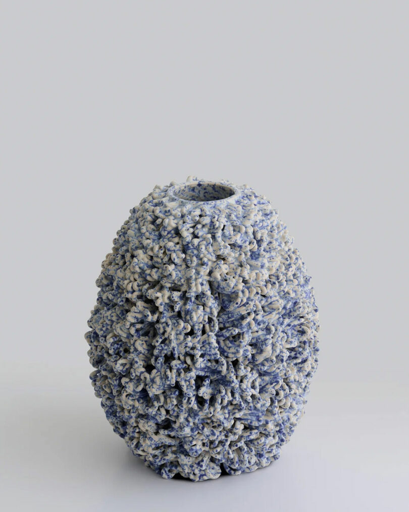Textured ceramic vase with a rounded, oval shape and a rough, spiky surface in blue and white tones, set against a plain light gray background.