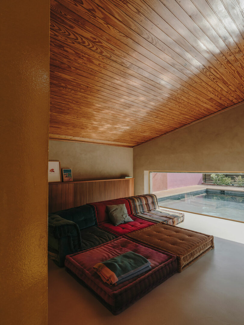 La acogedora sala de estar cuenta con un techo de madera, un sofá seccional en forma de L y grandes ventanales con vista a la piscina al aire libre y al patio.