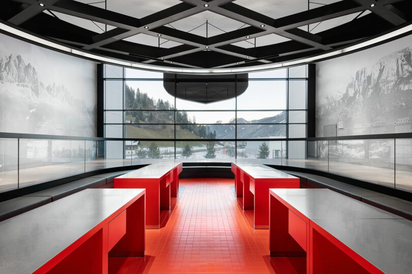 Modern interior with red tables, gray countertops, and large windows offering a view of mountains and trees in the background.