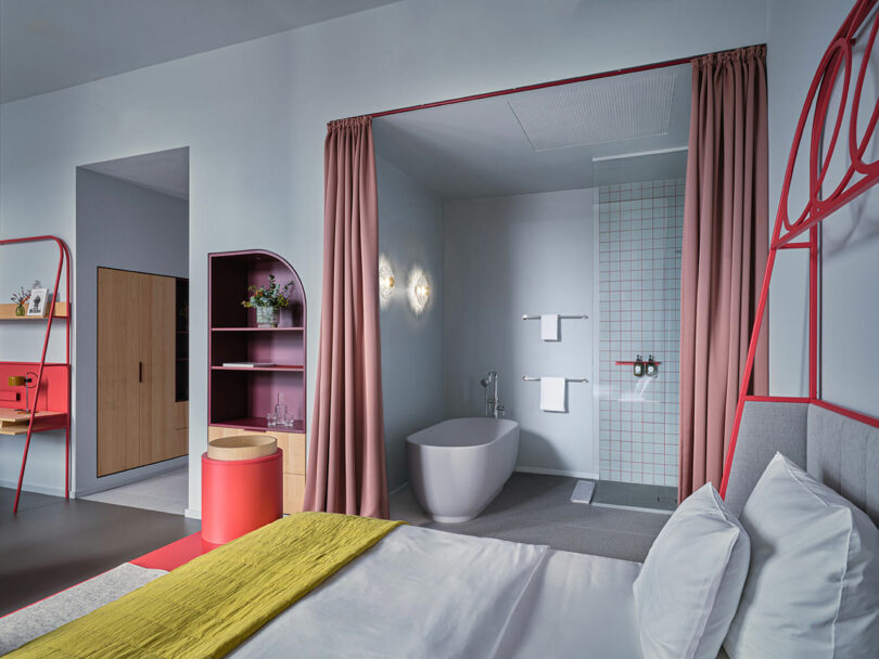 Modern NOXX Hotel room with a double bed, open bathroom area featuring a freestanding tub and shower, pink curtains, yellow bed throw, and contemporary decor elements.