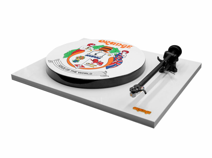 A white turntable with a crest design and the word "ORANGE" on the platter; tonearm positioned to the right; "Orange" logo on the bottom right corner of the base.