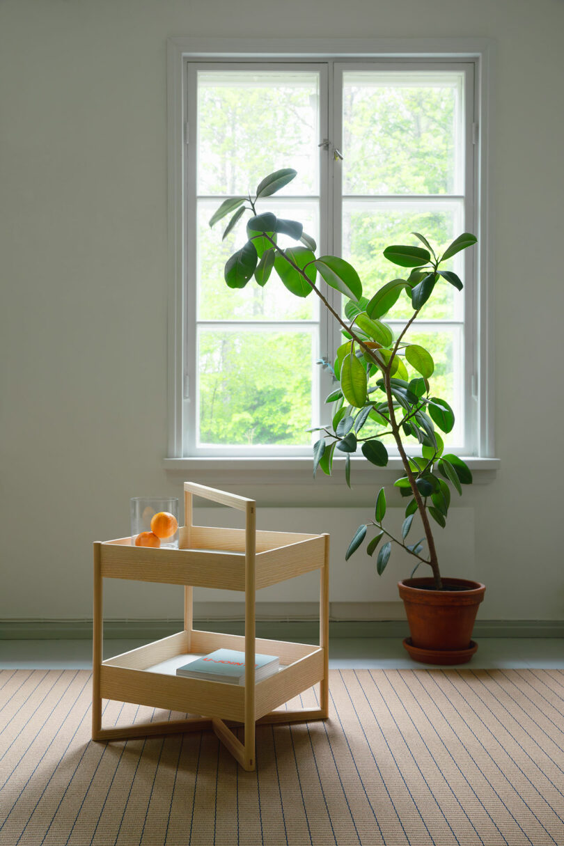 Nicari wooden side table with orange and glass at the top stands in front of the window, next to the hobbed on the striped mats in the light, minimum room.