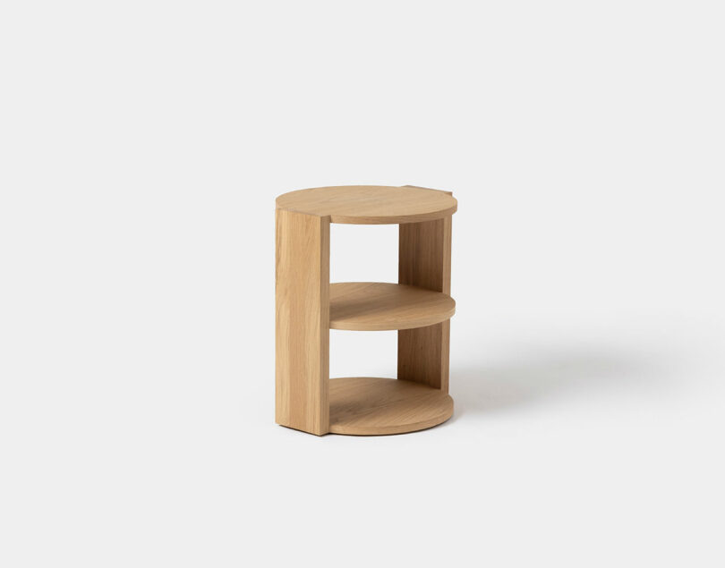 A small, round, light wood SCP-inspired side table with two open shelves and a simple, minimalist design, placed against a plain white background.