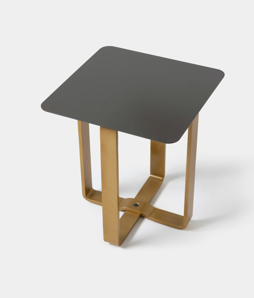 A small square SCP-inspired side table with a black top and intersecting gold metal legs, set against a plain white background.