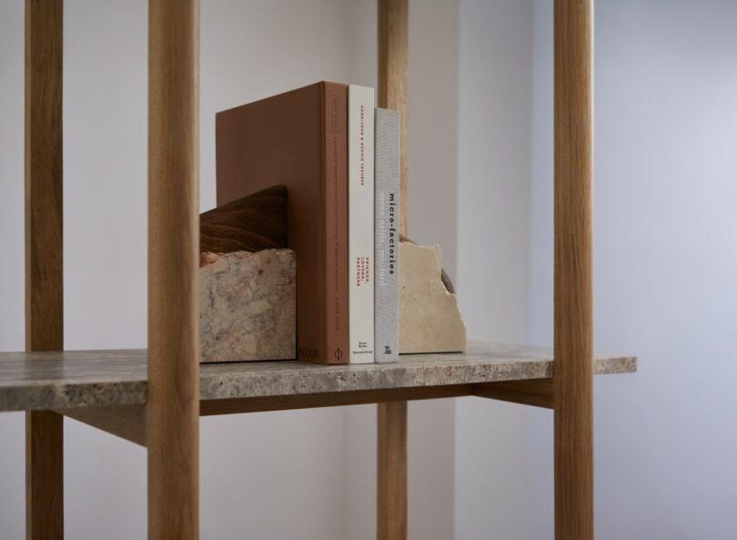 A shelf with three books standing upright between two stone bookends, framed by vertical wooden supports