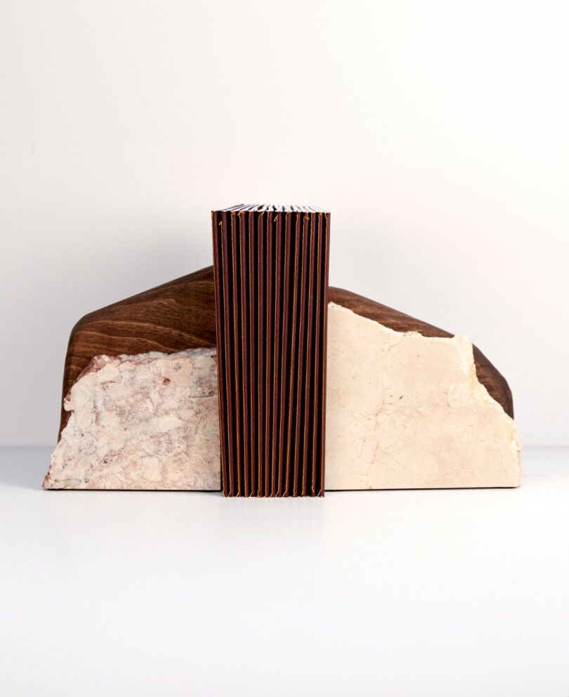 A geometric sculpture composed of two stone-like slabs on either side of a vertically ribbed, rectangular central piece, set against a plain white background