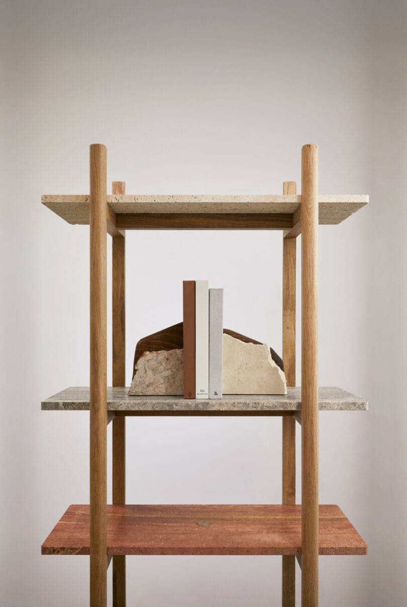 A wooden shelf with stone surfaces holds three upright books and two large rock pieces placed behind them, all against a plain, light-colored background