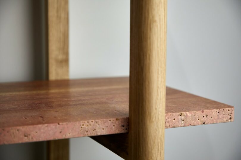 Close-up of a wooden shelf supported by two vertical wooden poles, with a natural, reddish-brown surface and a textured edge
