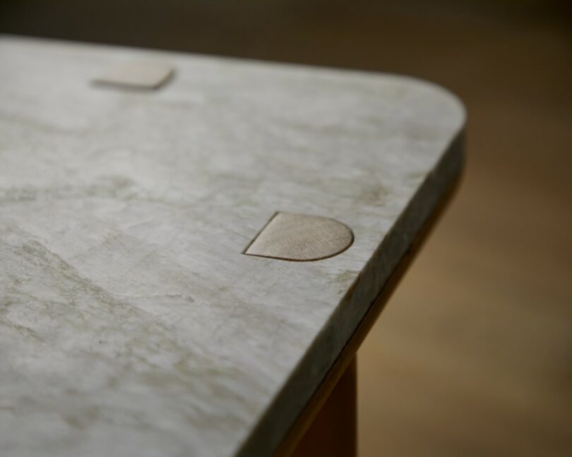 A close-up of a light-colored, rectangular marble tabletop with rounded corners and two semicircular wooden inlays near the edges