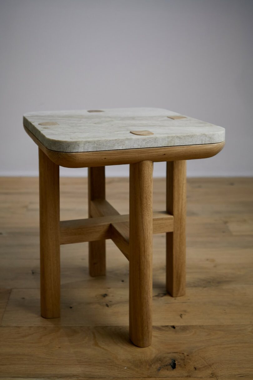A wooden chair with four legs and a light-colored square seat is placed on a wooden floor against a plain gray wall