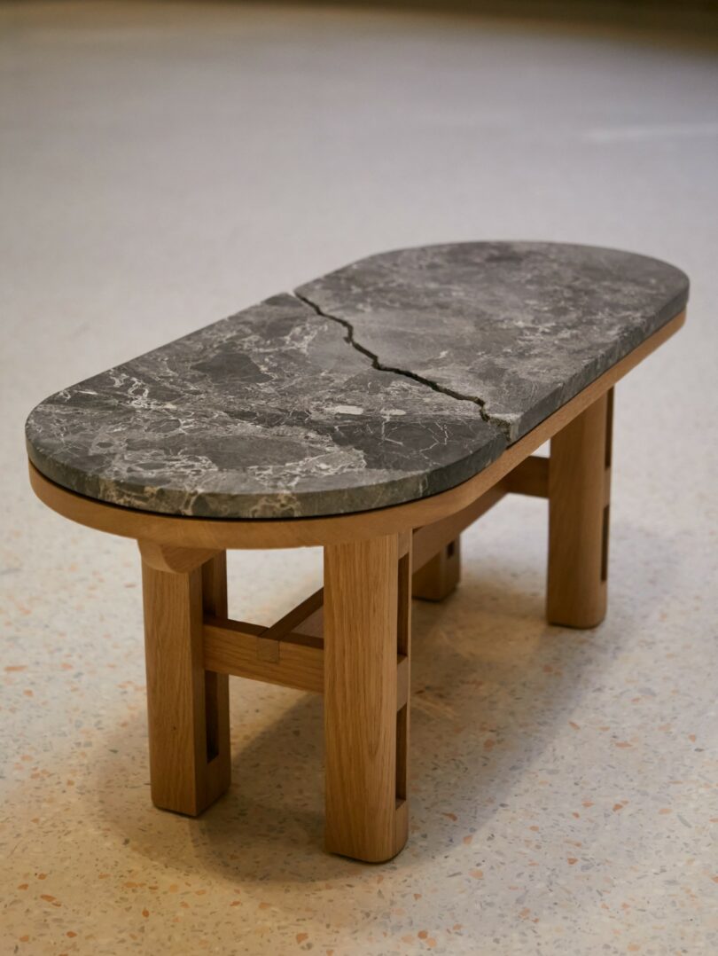 A small wooden bench with a cracked, dark gray marble top, standing on a light speckled floor