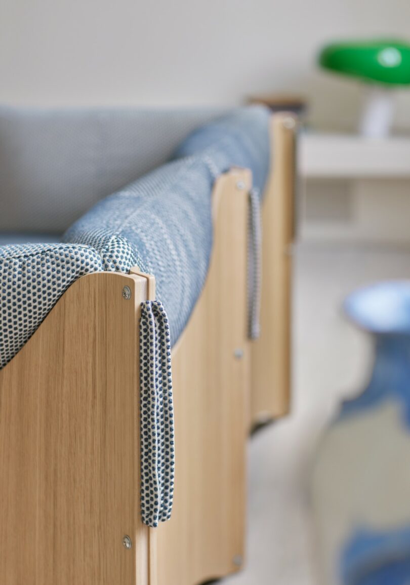 Primer plano de un mueble de madera con una cubierta de tela estampada azul junto a una lámpara verde y un jarrón azul y blanco con un fondo borroso