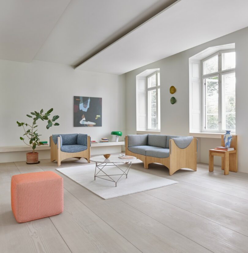 Salón moderno y minimalista con suelo de madera clara, dos sillones, una mesa de café, una alfombra, arte en las paredes, grandes ventanales y plantas en macetas.