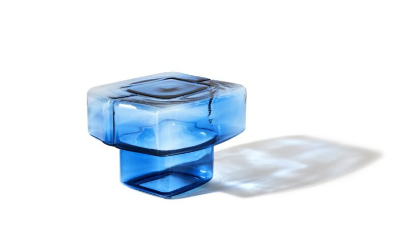 Blue glass object with a geometric, square design, casting a shadow on a white surface