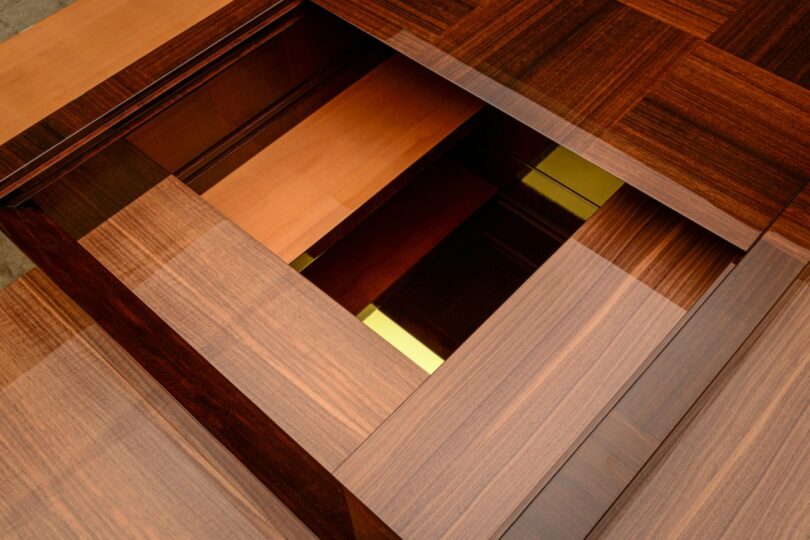 Vista cercana de una estructura geométrica de madera con paneles superpuestos, que revela secciones empotradas con adornos dorados y de madera clara.