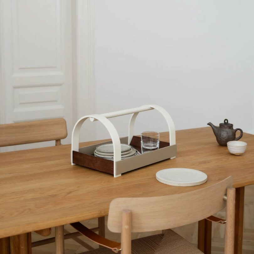 A wooden dining table with two chairs, holding a modern serving tray with plates and glasses, and a teapot set with cups nearby