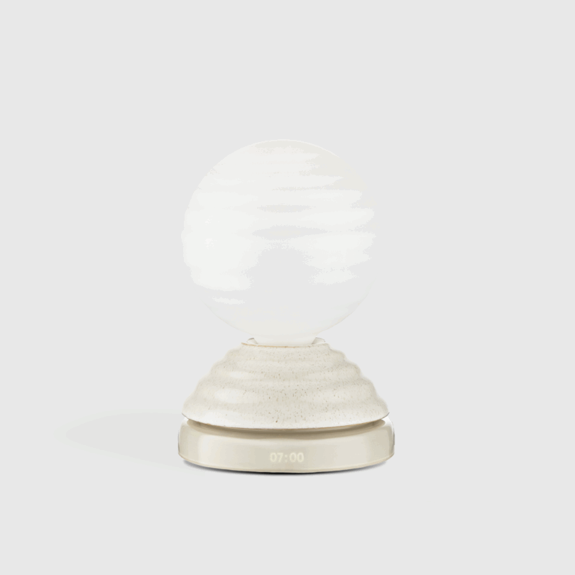 A modern white spherical lamp sits on a textured base with an LED display showing "07:00" on the front