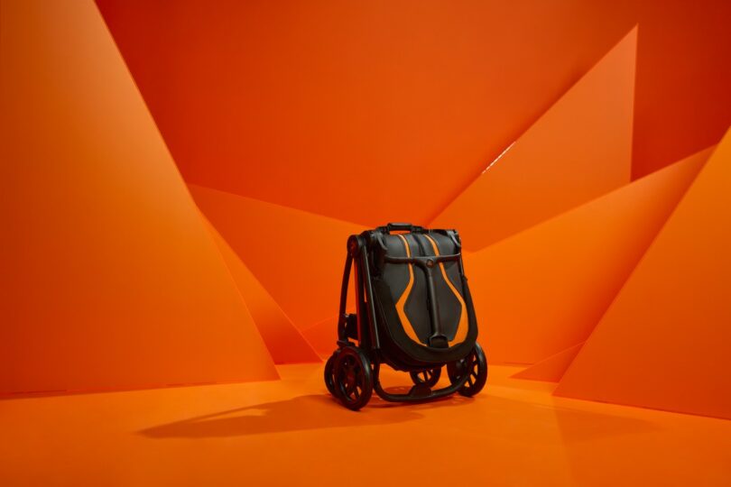 Close-up of a Silver Cross Lamborghini black stroller handle with stitching detail against an orange background.