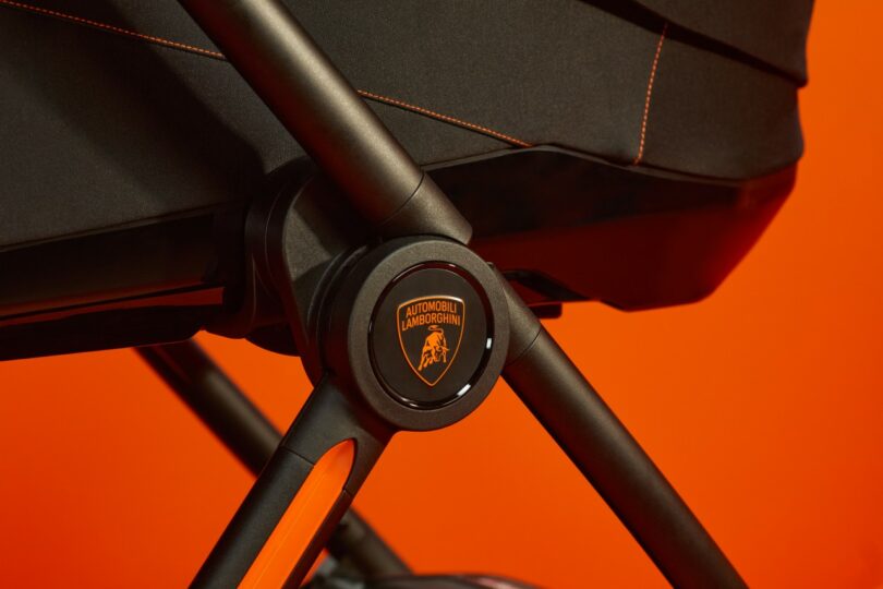Close-up of a Silver Cross Lamborghini black stroller handle with stitching detail against an orange background.