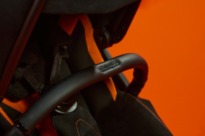 Close-up of a Silver Cross Lamborghini black stroller handle with stitching detail against an orange background
