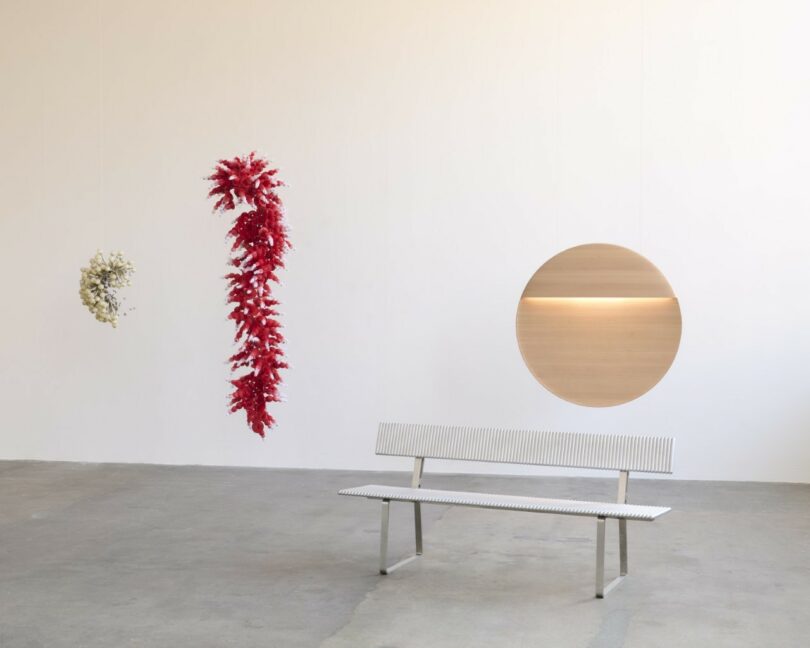 A variety of contemporary furniture and sculptural pieces are arranged in a minimalist gallery with white walls and a concrete floor