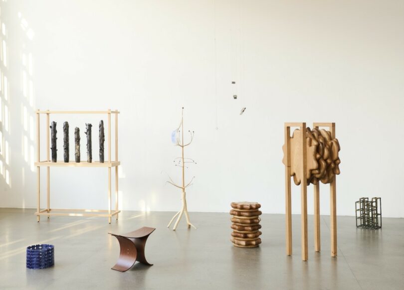 Una galería minimalista con paredes blancas y pisos de concreto está llena de una variedad de muebles y esculturas modernas.