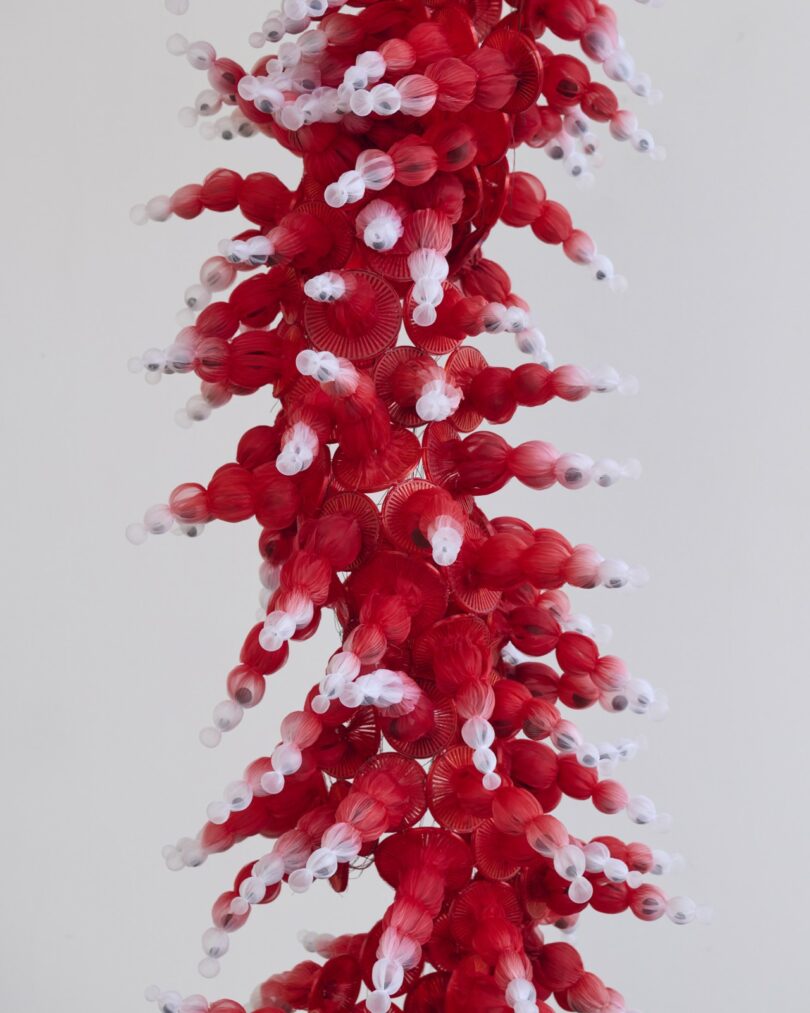 A close-up of a red and white spiral structure resembling a stylized DNA double helix model against a plain background