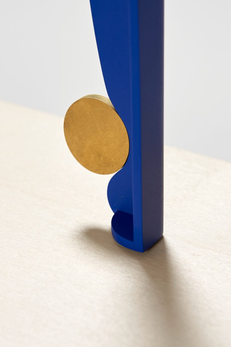 A close-up of a blue table leg with a round gold accent appears to tiptoe gracefully on a light-colored wooden surface
