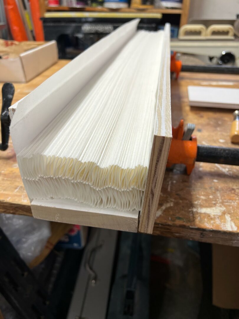A lamp in progress with folded paper sections clamped between wooden boards on a workbench.
