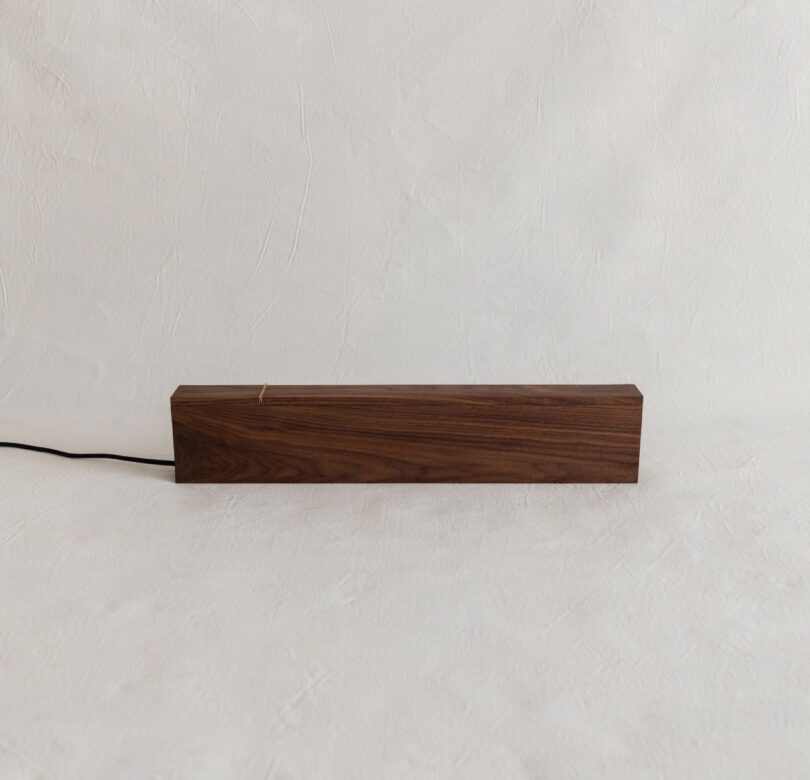 A rectangular wooden block with a visible cable sits on a white textured surface against a matching white background