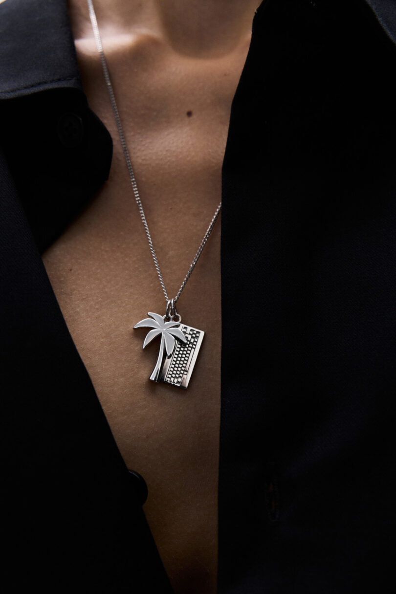 Un hombre con una camisa negra con el botón superior desabrochado mostraba un collar de plata decorado con una palmera y un colgante de teclado.