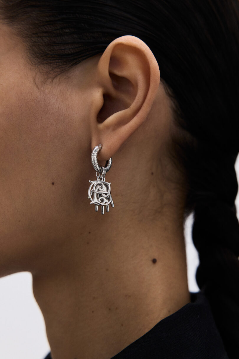Un primer plano de las orejas de un hombre, que lleva un arete de plata adornado con un diseño geométrico en forma de garra; el cabello es negro y trenzado.
